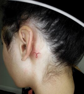 Aries Red Symbol Behind Ear Tattoo