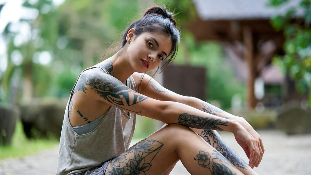 Woman with multiple arm and leg tattoos sitting outdoors in a natural setting