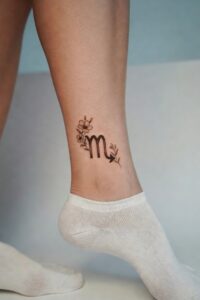 Floral Scorpio zodiac symbol tattoo on a woman’s ankle