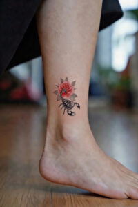Scorpion and red rose tattoo on a woman’s ankle