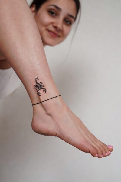 Small black scorpion tattoo on a woman’s ankle with minimalist fine-line design