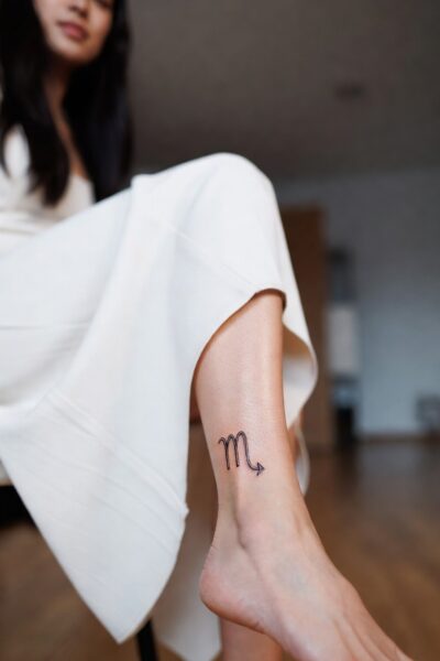 Small minimalist Scorpio zodiac symbol tattoo on a woman’s ankle